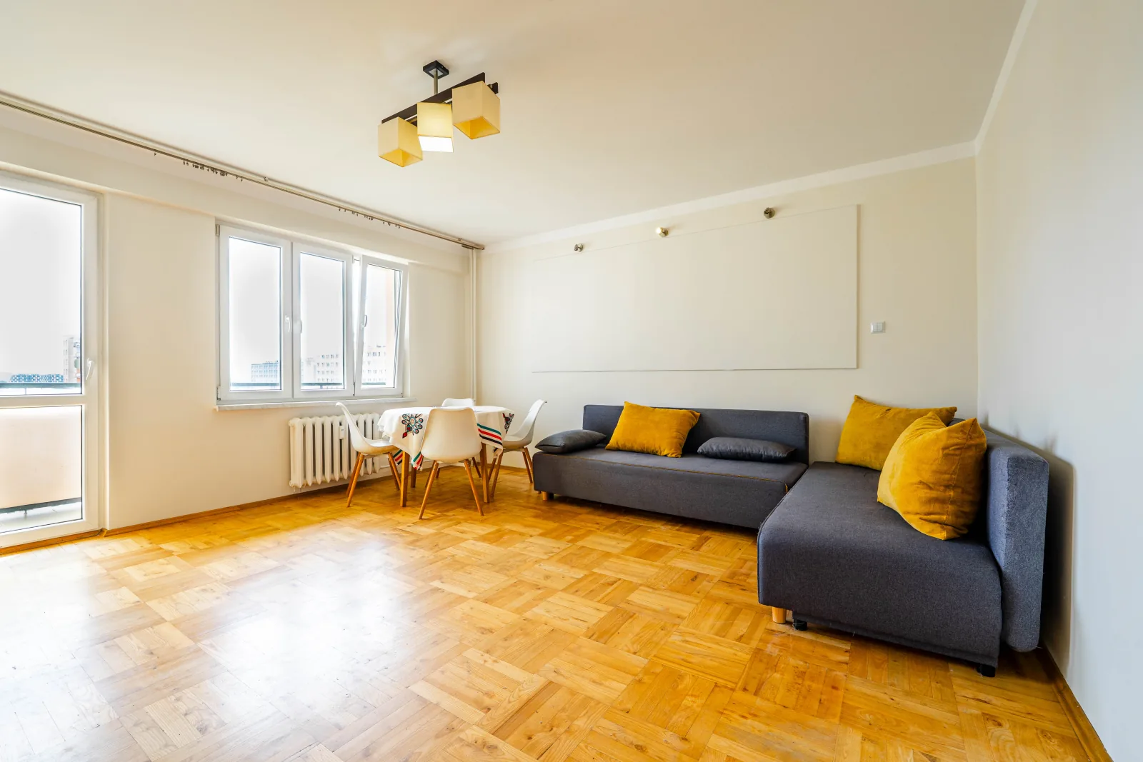 Salon z szarą sofą, parkiet i wyjście na balkon