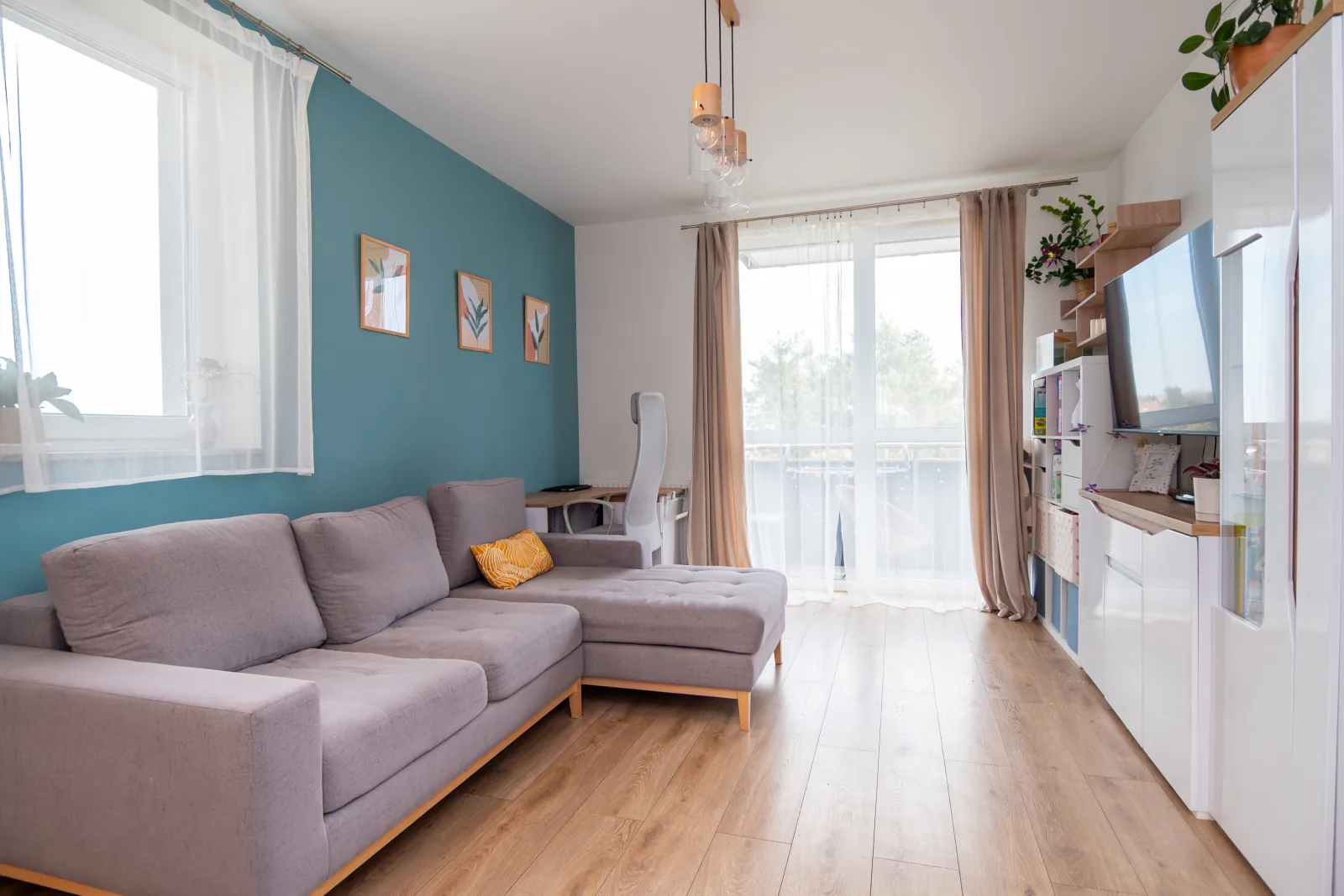 Salon z zieloną ścianą, szarą sofą i wyjściem na balkon