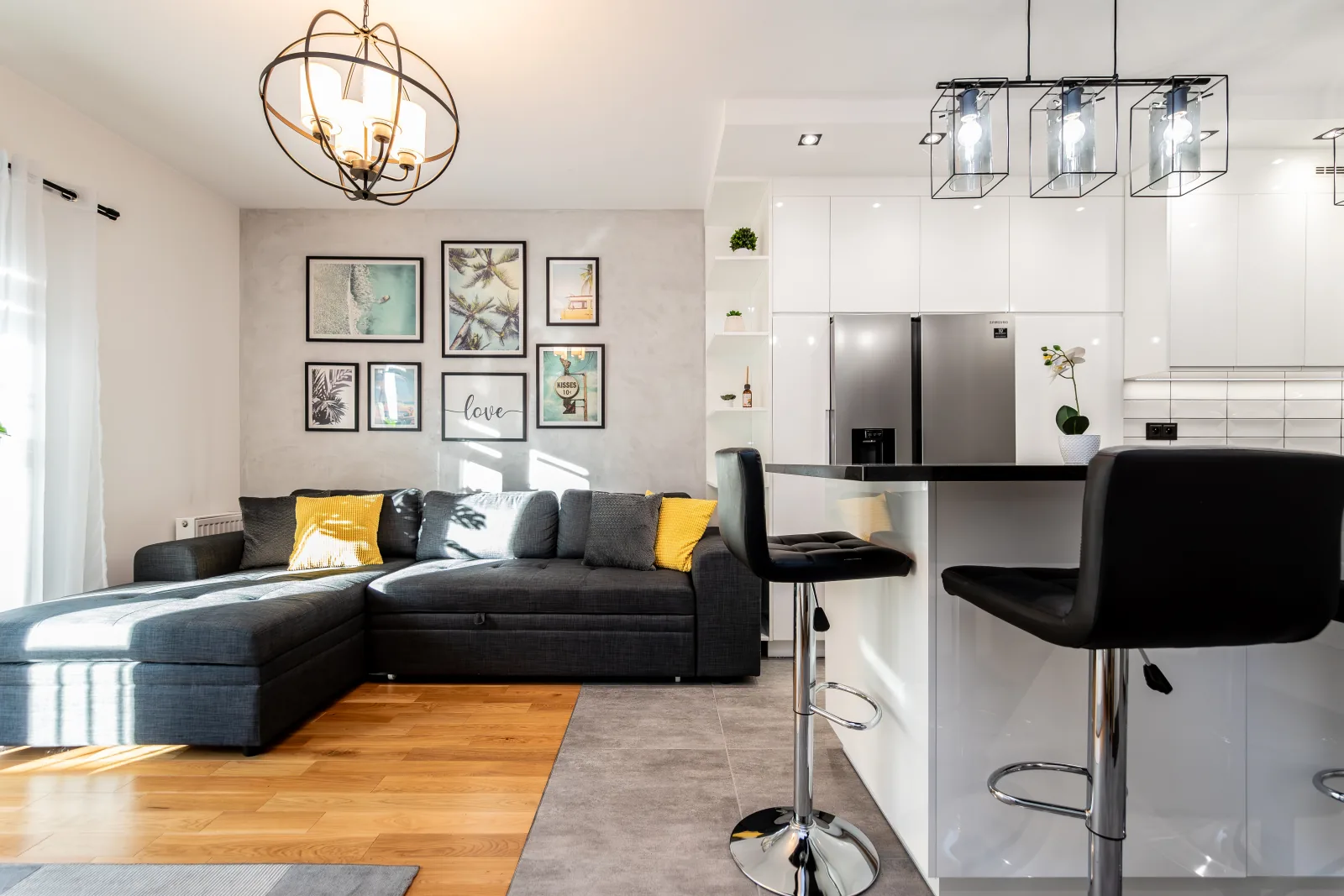 Salon z szarą sofą, galerią obrazków i białą zabudową kuchni