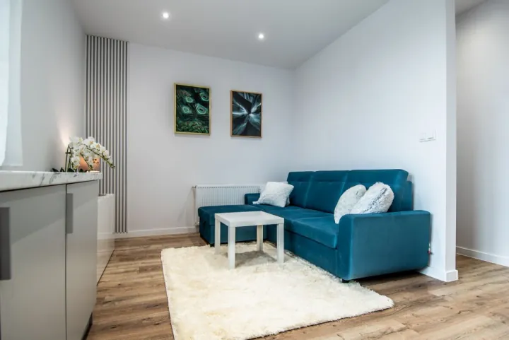 Salon z niebieską sofą, jasna zabudowa kuchni po lewej, Warszawa · Mokotów · Wierzbno
