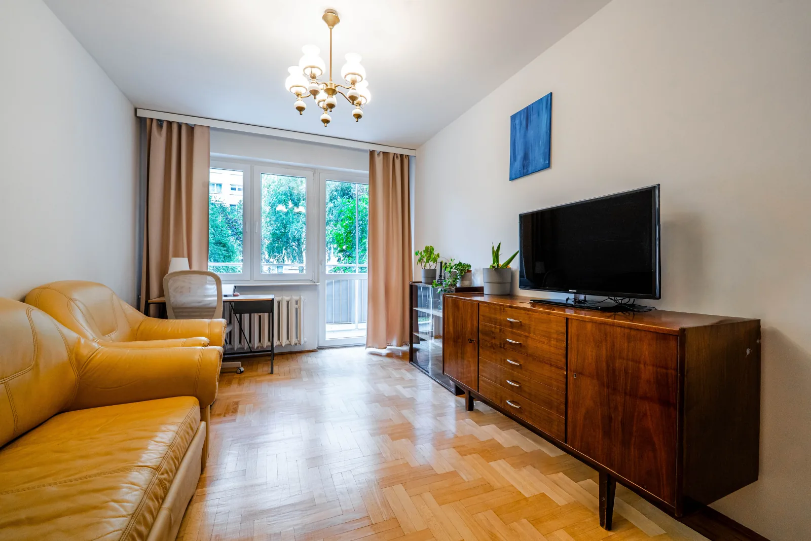 Salon z żółtą skórzaną sofą, telewizorem i wyjściem na balkon